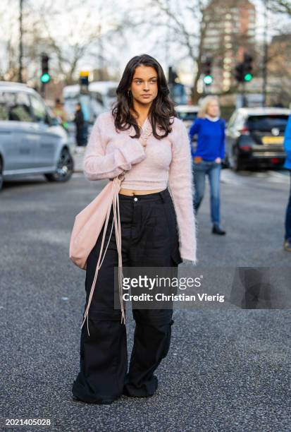 Nora Krog wears pink cashmere cropped jumper, black pants with side pockets, oversized rose pink bag outside Holzweiler during London Fashion Week...