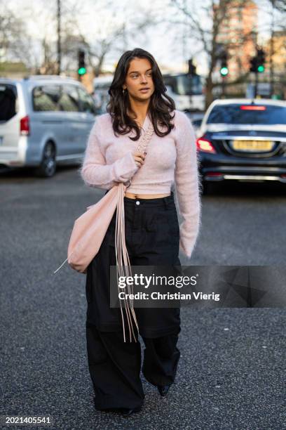 Nora Krog wears pink cashmere cropped jumper, black pants with side pockets, oversized rose pink bag outside Holzweiler during London Fashion Week...