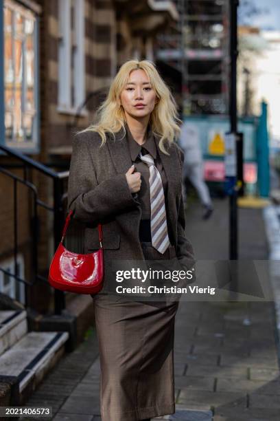 Betty Bachz wears brown jacket, tie, pants, shirt outside Eudon Choi during London Fashion Week February 2024 on February 18, 2024 in London, England.