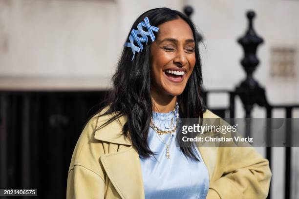 Zeena Shah wears blue bows in hair, blue dress, pearl necklace, beige coat outside Eudon Choi during London Fashion Week February 2024 on February...
