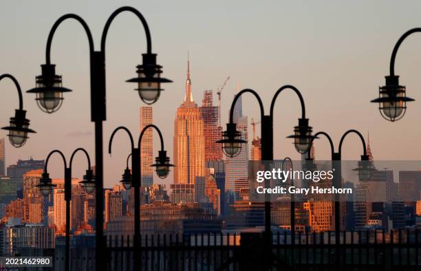 The sun sets on the skyline of midtown Manhattan and the Empire State Building in New York City behind lamp posts in Liberty State Park on February...