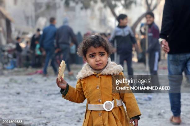 Graphic content / A Palestinian girl eats a piece of bread as people check debris on February 22 following overnight Israeli air strikes in Rafah...