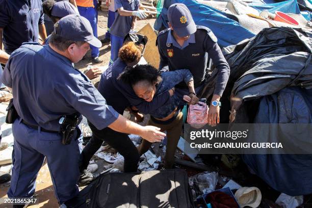 An homeless woman is removed from a makeshift shelter as South African policemen carry out an eviction order on February 22, 2024 in Cape Town, South...