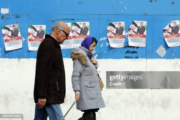 Man and a woman walk past electoral campaign posters bearing portraits of a parliamentary candidate during the first day of election campaign in...