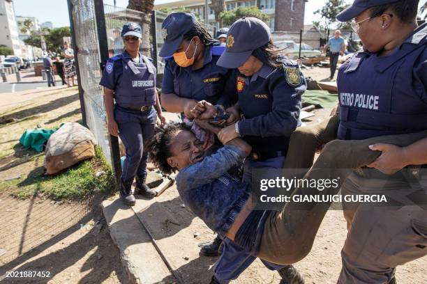 An homeless woman is removed from a makeshift shelter as South African policemen carry out an eviction order on February 22, 2024 in Cape Town, South...