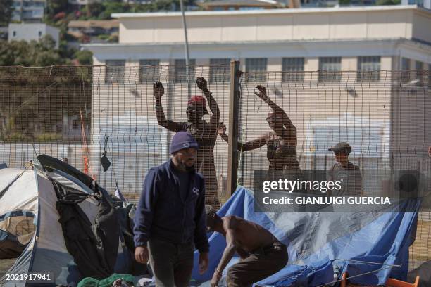 Homeless people look through a fence as South African policemen and City of Cape Town law enforcement and marshals take down makeshift shelters as...