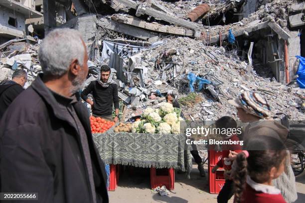 Vendors wait for customers at a food market in front of destroyed buildings in the Nuseirat refugee camp in Nuseirat, central Gaza, on Tuesday, Feb....