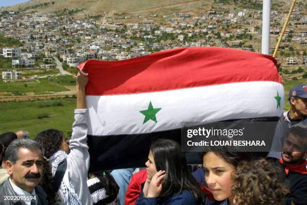 Syrians hold up a national flag 17 April 2001 in Ain Tineh, on the Syrian side of the Israeli-occupied Golan Heights, as they face the Druze village...