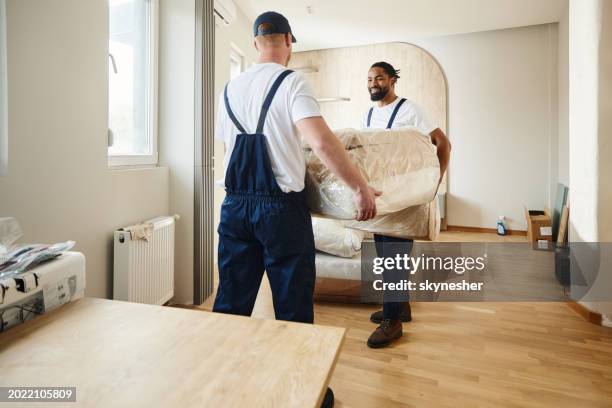 happy male movers carrying furniture in the apartment. - mover stock pictures, royalty-free photos & images