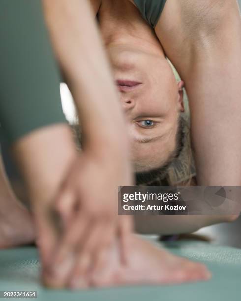 woman does yoga on mat. parivrtta prasarita padottanasana. woman's face in upside down asana position. stretching. pilates. upside down exercise. torso in twist. close-up. soft focus - revolved triangle pose stock pictures, royalty-free photos & images