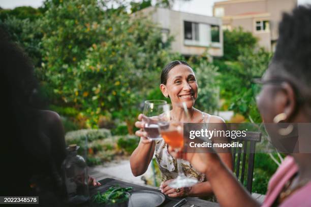 smiling women toasting together with drinks during a patio dinner party - dusk stock pictures, royalty-free photos & images