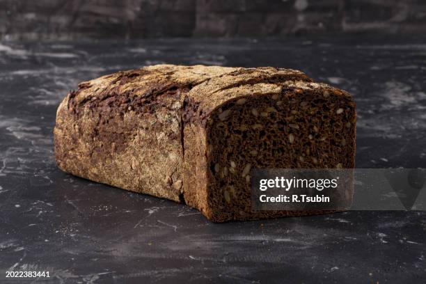 rye black bread with seeds on dark board background - rye grain stock-fotos und bilder
