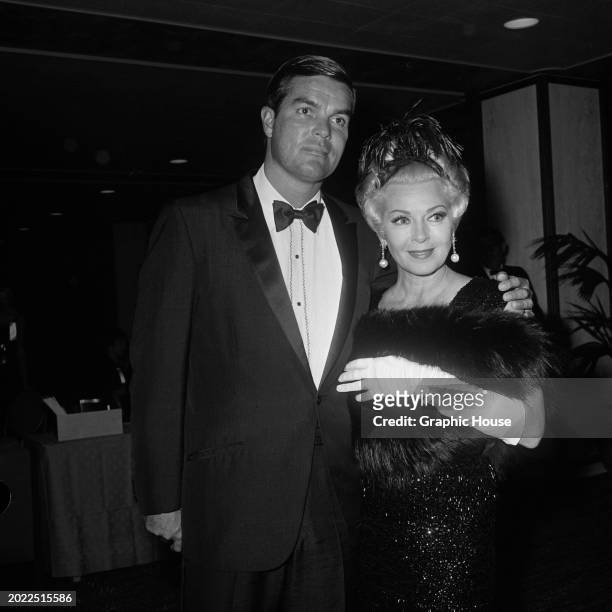 American film producer and businessman Robert Eaton, wearing a tuxedo and bow tie, with his wife, American actress Lana Turner, who carries a fur...