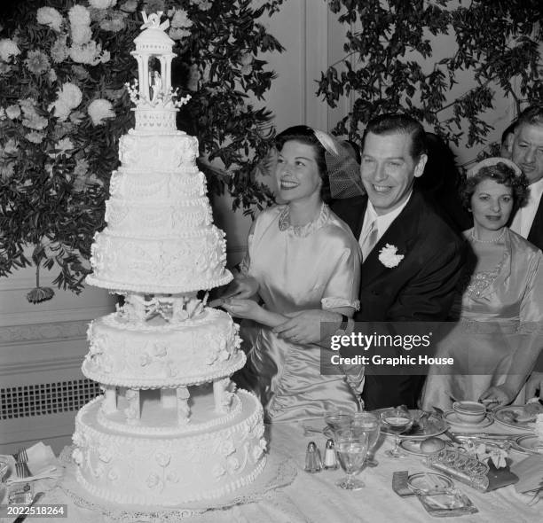 American publicist Ruth Cosgrove and her husband, American comedian Milton Berle cutting their wedding cake at their wedding reception, held at The...