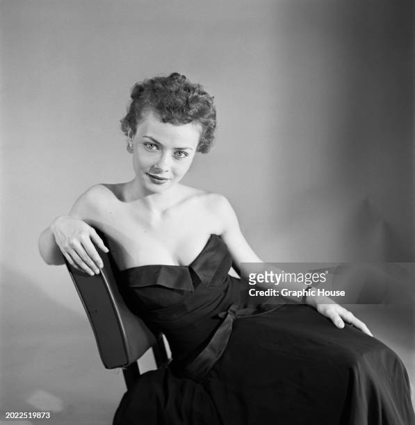 Model wearing a black strapless evening gown, with a sweetheart neckline, sits with her right arm resting on the backrest of her chair, United...