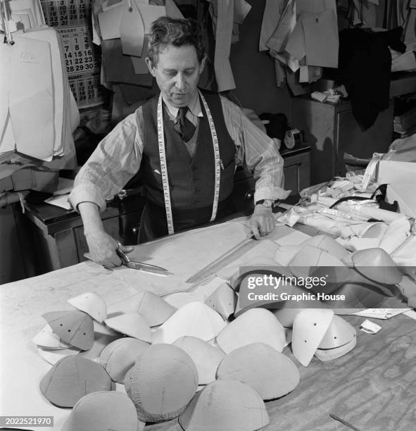 Cutter, a tape measure draped around his neck, cutting patterns as he prepares cups during the manufacturing process of bras, United States, circa...