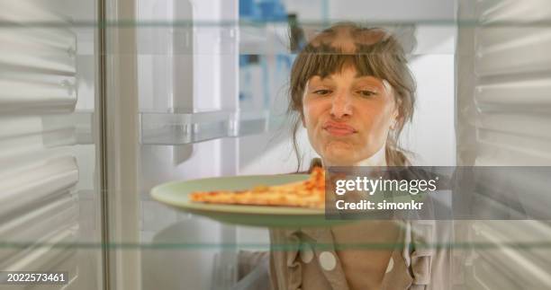 frowning woman looking slice of pizza - pizza temptation stock pictures, royalty-free photos & images