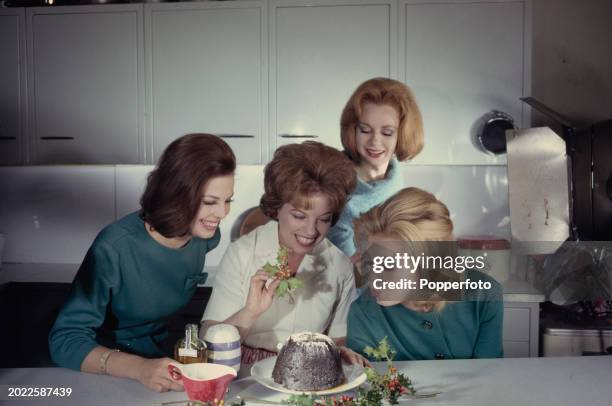 Four women gather round to place a sprig of holly on top of a Christmas pudding in a kitchen in London on 22nd December 1962.