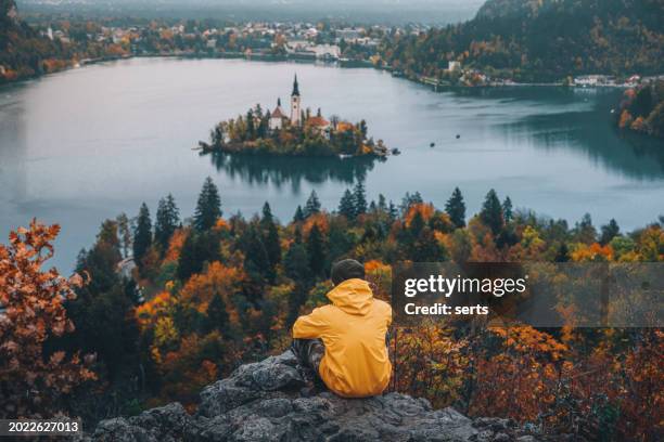 giovane viaggiatore e avventuriero con impermeabile giallo gode della vista aerea del lago di bled (blejsko jezero) dal monte osojnica in slovenia - bled foto e immagini stock