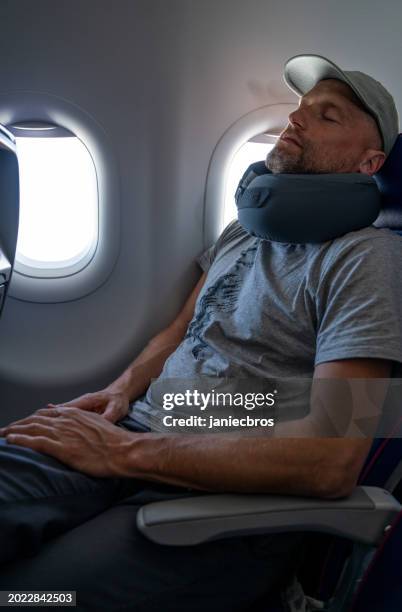 ein mann ruht sich mit einem kissen im flugzeug aus - flugzeug schlafen stock-fotos und bilder