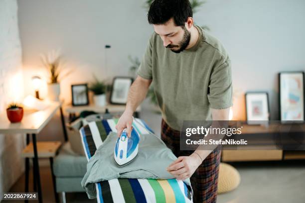 young man ironing - tábua-de-passar-roupa imagens e fotografias de stock
