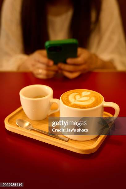 cup of coffee latte on a red table with human hands using smart phone background. - coffee table reading mug stock pictures, royalty-free photos & images