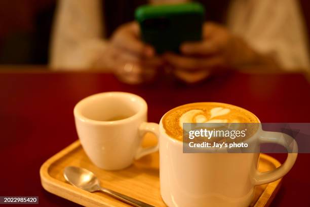 cup of coffee latte on a red table with human hands using smart phone background. - coffee table reading mug stock pictures, royalty-free photos & images