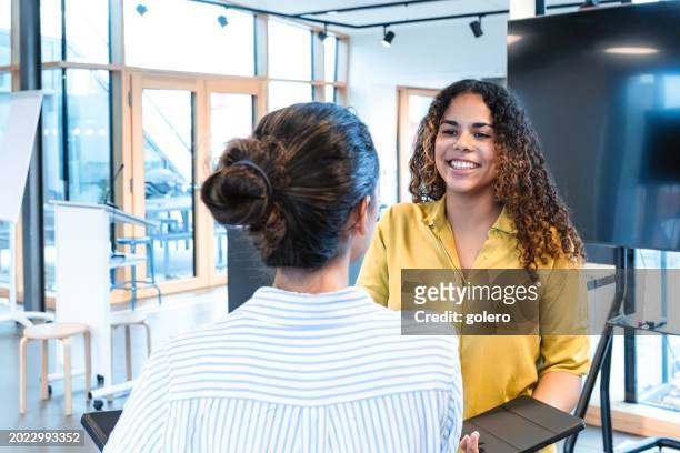 young smiling woman with digital tablet talking to another woman - woman 20 summit in berlin stockfoto's en -beelden