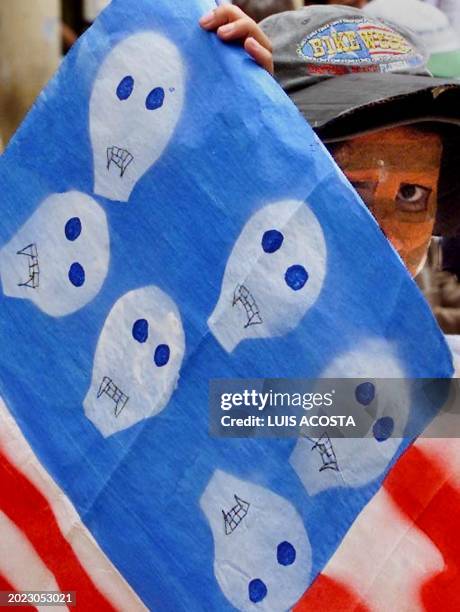College student, with his face painted, hides behind a flag mocking the one of the United States, in Bogota, Colombia, 01 May 2001, during a march...
