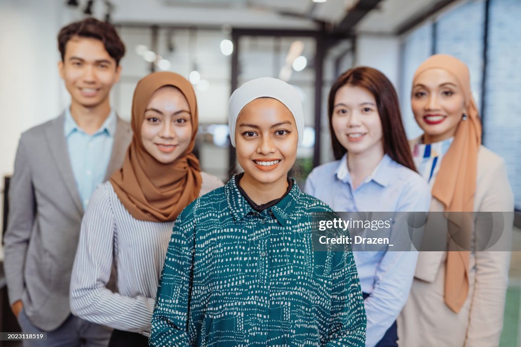 Successful group of business people in modern office, looking at camera and smiling. South-East Asian and Chinese business people. Focus on young businesswoman