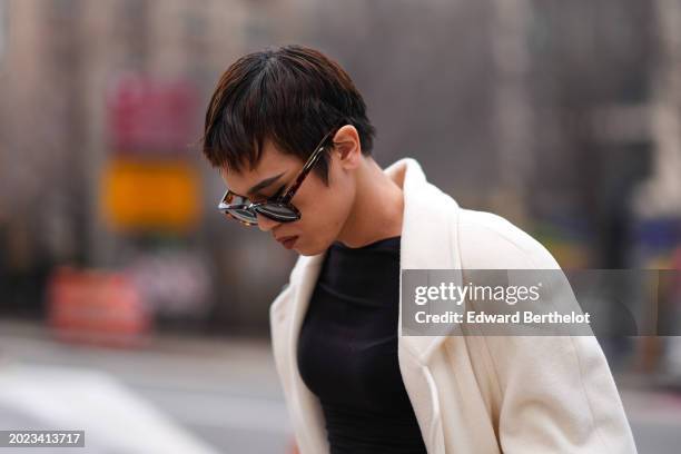 Guest wears brown sunglasses, a white long coat, a black dress, outside Eckhaus Latta, during New York Fashion Week, on February 10, 2024 in New York...