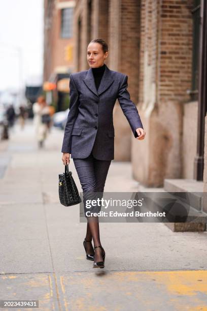 Guest wears a black turtleneck pullover, a gray oversized blazer jacket , a skirt, a black woven leather bag, tights, black pointed shoes, outside...