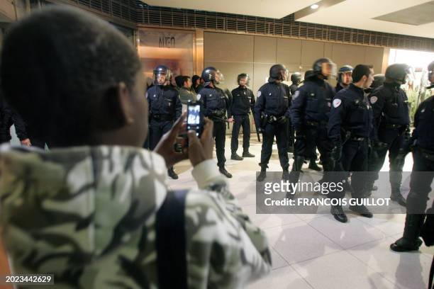 Young boy takes a picture with his mobile as police officers stand guard during riots at the Paris Gare du Nord railways station, 27 March 2007....