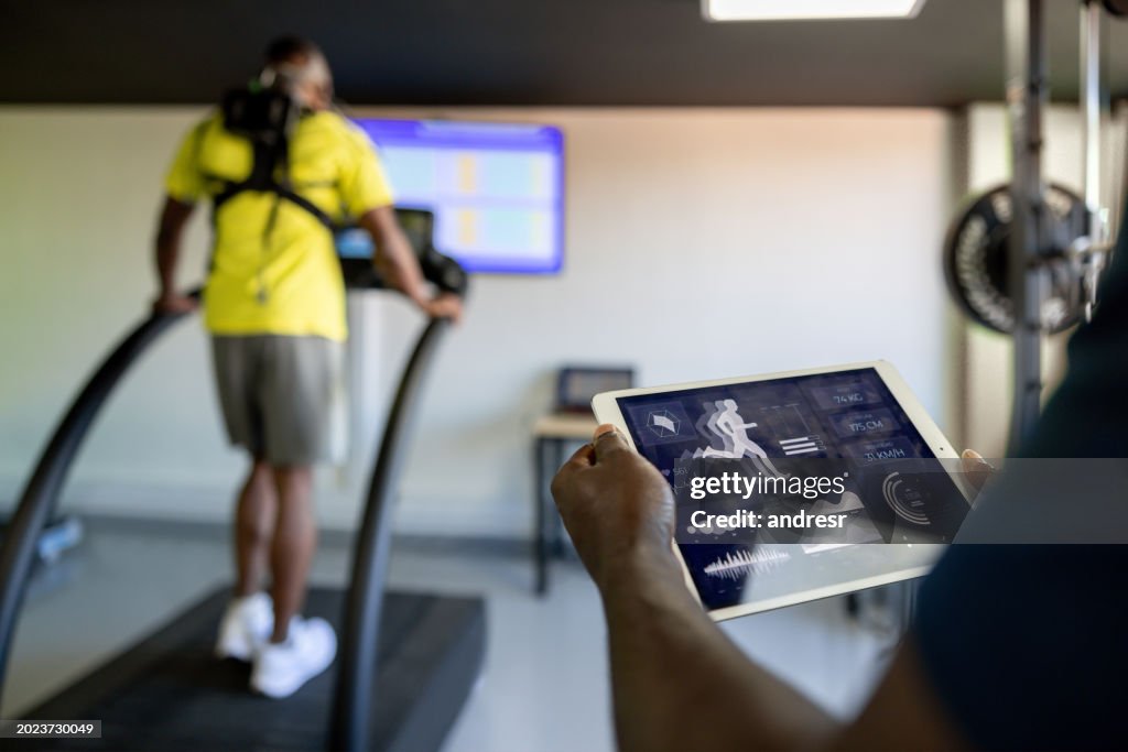 Instructor de fitness usando una tableta mientras realiza una prueba física en un gimnasio
