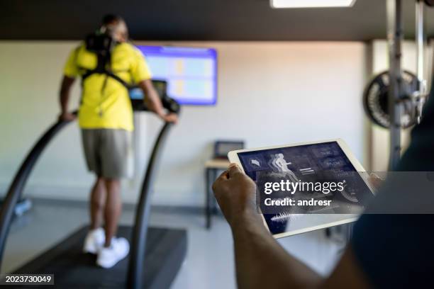 fitness instructor using a tablet while performing a physical test at a health club - stress test stock pictures, royalty-free photos & images