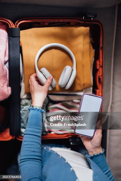 packing essentials for a trip: headphones, clothes, and a smartphone in a suitcase - travel essentials stock pictures, royalty-free photos & images