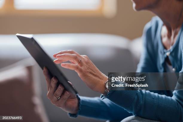 senior woman engaged in reading on digital tablet at home - multimedia learning stock pictures, royalty-free photos & images