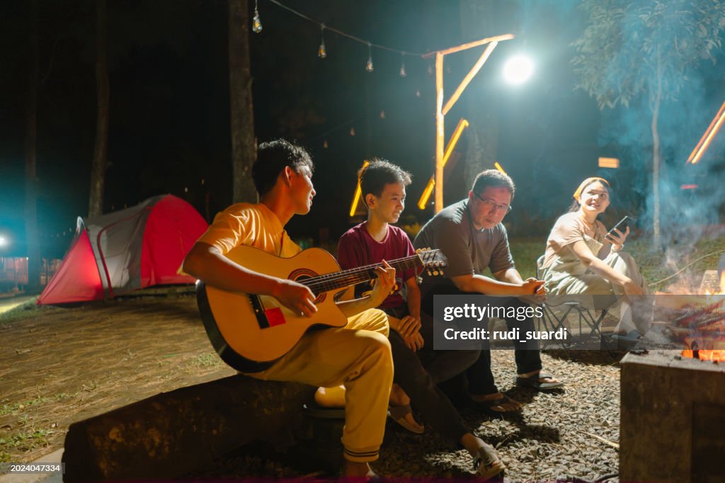 Group of friends having fun playing guitar while camping at the night
