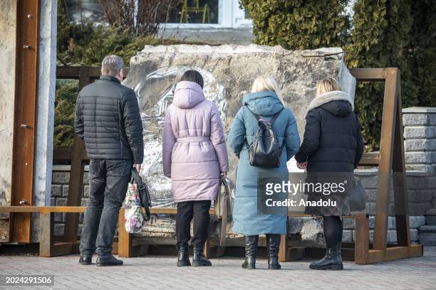People look at a stone as Kyiv Oblast, surrounding the capital of Ukraine, still bears the scars of the war as the country marks the 2nd anniversary...