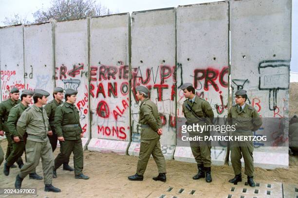 East German border guards stand guard as other demolish a section of the Berlin Wall, between East berlin and the no-man's-land, to open a new...