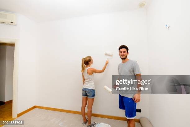 pareja joven pintando pared en una casa nueva - wall painting couple fotografías e imágenes de stock