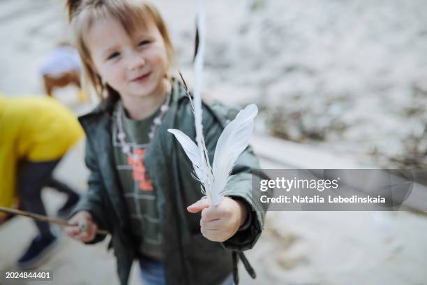 young girl picks up feathers at the lake shore, walks and discovering nature with children. - spotted lake stock pictures, royalty-free photos & images