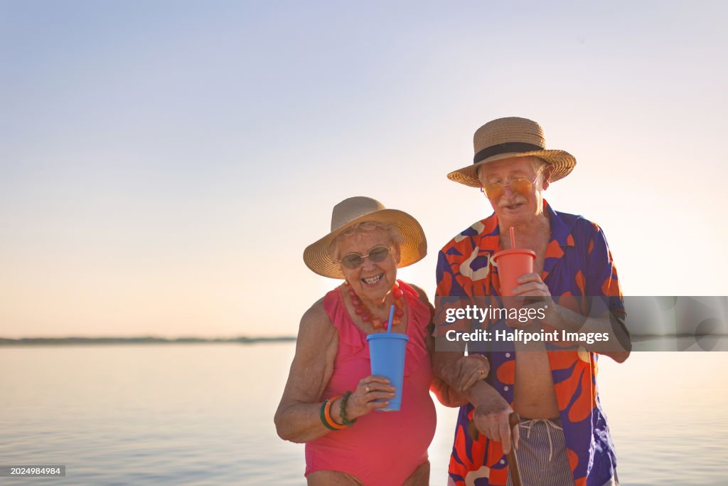 Pensioners having fun on the beach, holding hands and walking through the water Beach party with cool elderly couple. Senior newlyweds on their honeymoon. Concept of traveling in retirement.