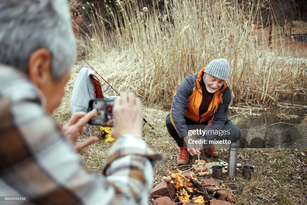 Senior woman taking photo of her husband while camping together in nature