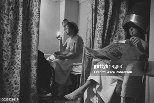 Client lights up a cigarette as another reads the paper while under a hair hood in the changing room at the Savoy, a women's Turkish bath on Duke of...