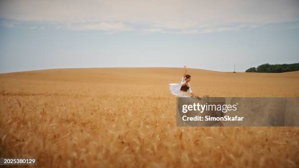 carefree woman with one arm raised riding bicycle amidst wheat field - hungary countryside stock pictures, royalty-free photos & images