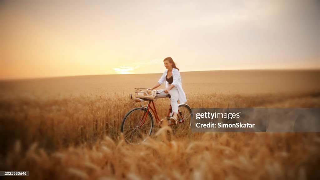 Happy Woman Enjoying A Bicycle Ride Amidst Wheat Field
