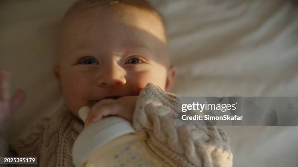 close-up of cute happy baby boy with milk bottle lying in crib - milk bottle stock pictures, royalty-free photos & images