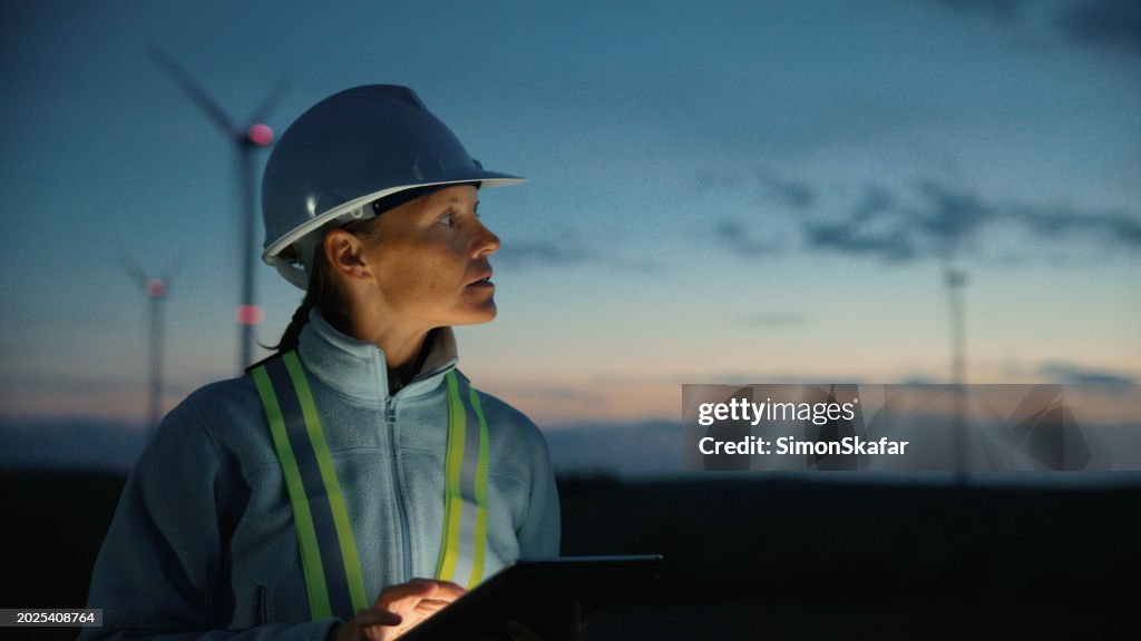 Engineer Woman Checking Wind Turbines on Tablet at Dusk