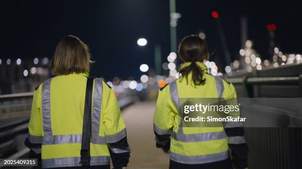 ingenieras con ropa reflectante caminando por un puente iluminado por la noche - material reflector de seguridad fotografías e imágenes de stock